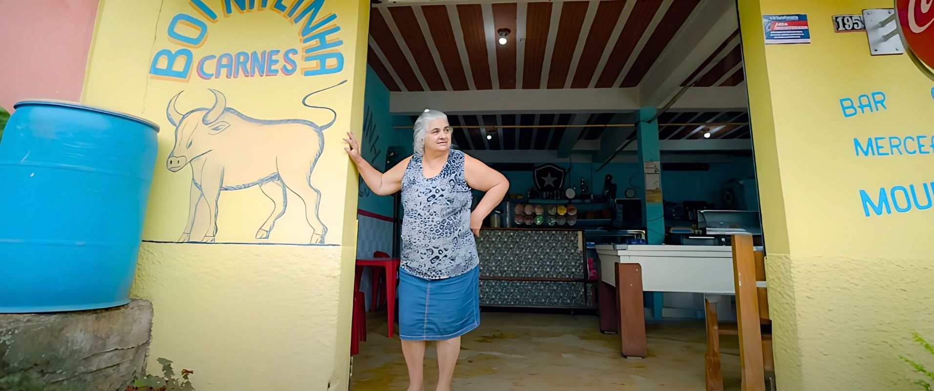 Mulher de 67 anos em pé em frente ao seu comercio